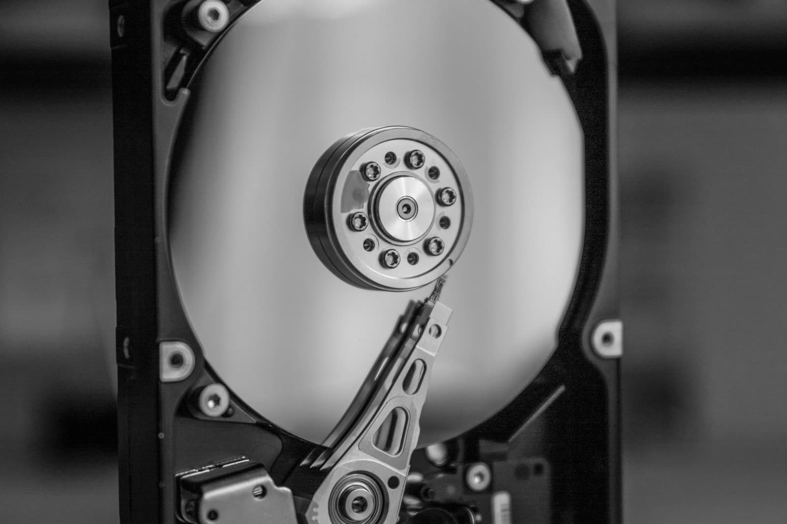 A close-up of an opened hard disk drive showing the reflective platter, spindle, and read arm against a dark background