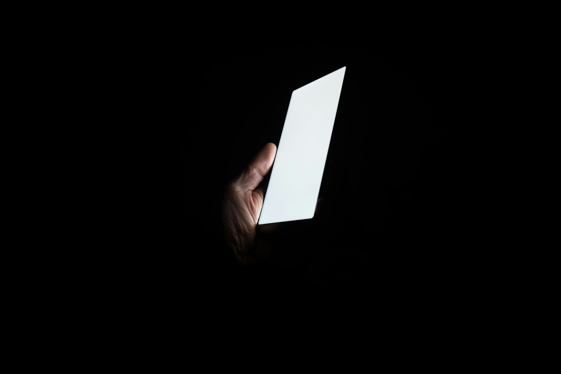 A single hand holding a smartphone with a glowing screen in a dark room